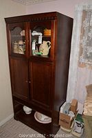 Front view of tall dark brown solid wood entertainment center cabinet showing upper glass doors, lower wooden doors, and open bottom shelf with some decorative items.