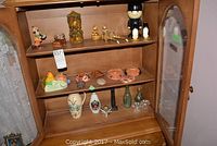 Wide view of wooden cabinet shelves with various decorative items including ceramics, figurines, glassware, and masks.
