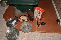 Lot showing Bell and Howell binoculars in case, wooden guinea hen, fish thermometer, rooster clock ornament, and three metal wall plaques on floor.