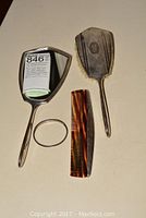 Top view of the silver hand mirror, silver hairbrush, folding comb and silver bracelet laid out on a surface.