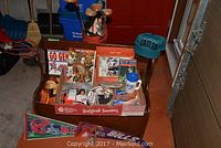 Wooden chest filled with sports collectibles and memorabilia including framed Blue Jays items, Eagles cap, Buffalo Bills pennant, and sports cards arranged around the chest