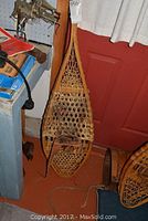 Pair of large wooden framed snowshoes leaning against a red door, showing full length and shape