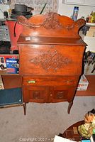 Full front view of wooden secretary desk with carved crest and closed drop-front