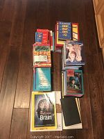 Top view of the books showing titles like Larousse dictionary, Nancy Drew series, The New Science of the Brain, and other assorted books stacked together on a wooden floor.