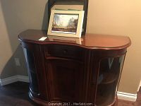 Front view of the wooden hutch with glass top and one art print leaning on it.
