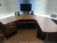Corner desk showing the full L-shape with wood grain finish, two drawers on left side, keyboard tray in middle, and visible surface damage.