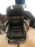 Front view of the black faux leather office chair showing the seat, backrest, and armrests with wear on the right armrest.