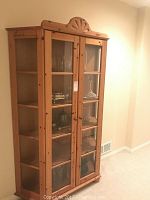 Front view showing the full height pine display cabinet with two glass-paned doors and interior shelving. Decorative carved wood top visible.