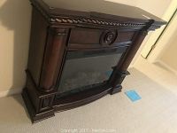 Front-left side view of dark wood electric fireplace mantel, unit standing on carpet, insert unlit