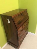 Side angle showing the closed secretary desk with three large drawers and a slanted fold-down writing surface in a dark wood finish.
