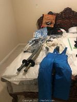 Costumes and snow pants laid out on bed including the blue snow pants, plush cow costume, witch costume, two toy swords, and a bag with Halloween graphics.