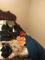 Pile of assorted costumes including butterfly costume wings, black and red/orange dress, blue snow pants, and additional pieces laid on a bed.