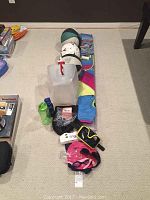 Wide shot of assorted sporting goods laid out on carpet, including swim goggles, swim cap, stunt glider kite, water bottles, and plastic container.