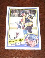Front of Doug Gilmour rookie card showing image of player in blue and yellow Blues uniform on ice and portrait inset.