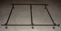 Full view of the metal bed frame laid flat on the floor, showing rectangular structure and caster wheels at each corner