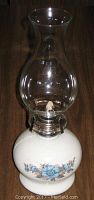 Front view of white ceramic oil lamp with blue floral pattern and clear glass chimney in place.