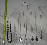 Photo of seven assorted costume jewelry necklaces laid out with measuring tape for size reference.