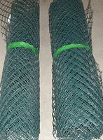 Two rolled lengths of green plastic chain link fencing lying side by side on a concrete floor, each secured with green ties.