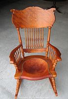 Front view of wooden rocking chair showing carved backrest and sunken leather seat with nailhead trim.