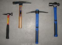 Four different hand tools photographed from above on a concrete floor: a claw hammer with wooden handle, ball peen hammer with black/red grip, pick hammer and cross peen hammer both with blue/black grips.