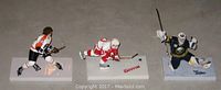Photo of three 6-inch hockey figures - Clarke, Datsyuk, and Miller, arranged side-by-side on a flat surface showing full body and base with player names.