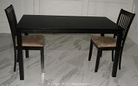 Dark brown rectangular wooden dining table with two chairs positioned on either side on a marble floor. Table surface is flat and legs square with some wear visible on corners.