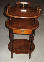 Front view of the vintage wood side table showing three tiers and drawer closed