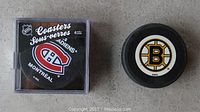 Photo showing the front of the sealed Montreal Canadiens coasters package alongside the Boston Bruins hockey puck.