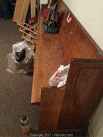 Side view of a long wooden bench with items placed on top, showing its length and center support.