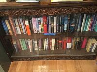 Two shelves of mixed genre books behind glass doors in a carved wooden bookcase.
