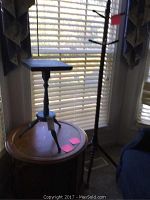 Wide shot showing a tall wooden coat rack, round wooden table with a smaller blue occasional table on top near window blinds.