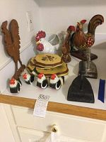 Overall view of the lot showing ceramic rooster figurines, napkin rings, serving trays, and cast iron door stoppers