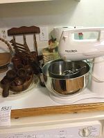 West Bend stand mixer in white with stainless steel bowls and several wooden kitchen decor items including napkin rings, napkin holder, and salt and pepper shakers.