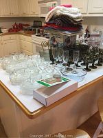 Kitchen counter showing glassware, dessert cups, place mats stacked, and boxed Hamilton Beach ice cream maker.