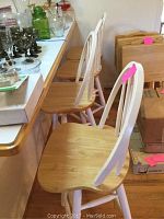 Four wooden swivel bar stools with white spindle backrests and legs, natural tan wood seats, arranged side by side at a counter.