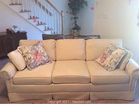 Front view of cream Tradewinds sofa with two floral cushions on each end.