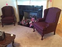 Two dark burgundy wingback armchairs with carved wooden feet, shown near a fireplace and living room setting.