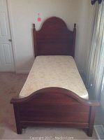 Full view of the twin bed with mattress showing wood frame with arched headboard and footboard.