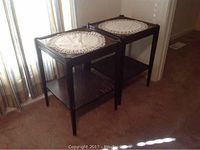 Full view of two dark wooden end tables side by side showing lace doilies on top and lower shelves, situated next to window with vertical blinds.