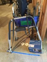 Photo showing adult collapsible wheelchair with blue seating and walker with storage apron in front. DeVilBliss nebulizer system box is on the ground by the walker.