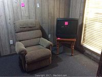 Photo showing La-Z-Boy recliner chair, side table, and Sharp TV in a room with wood panel walls and carpeted floor.