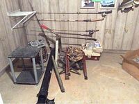 Fishing rods mounted on wall rack, tackle box on floor, portable chairs folded, small portable table, rod tubes on floor.