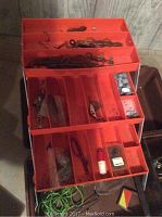 Open brown plastic tackle box showing orange multi-compartment trays filled with assorted hooks, sinkers, swivels and bobber.