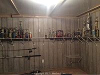 Wide shot of trophies arranged on two wall shelves with fishing rods mounted below. Wooden panel wall background.