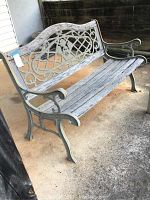 Full view of metal garden bench with wooden slats on seat and backrest, showing wear and weathering on wood and metal frame