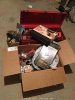Open red metal tool box with various hand tools and a box of screws in front