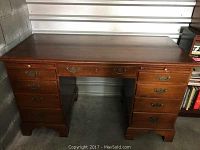 Front view of wooden office desk showing 8 drawers with brass handles.