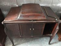 Front view of the antique Victrola cabinet phonograph showing two central doors, one door missing on the right side, curved legs, and wooden top with wear.
