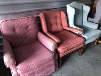 Three chairs side by side: a light blue wing chair on the right and two different red upholstered armchairs on the left and middle.