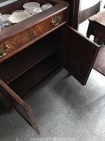 Open wooden cabinet doors revealing interior space and lower shelf beneath the drawer